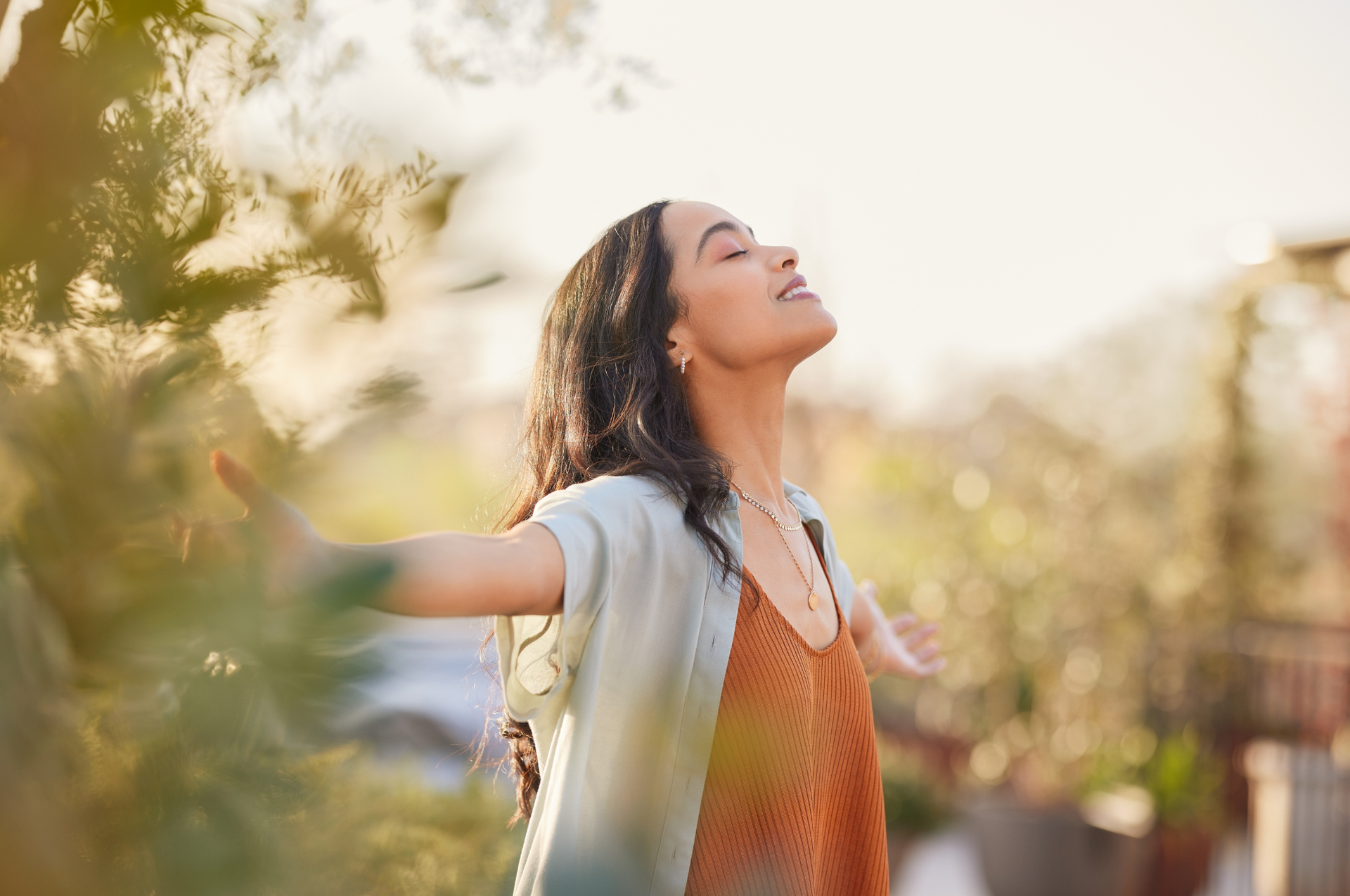 A woman is standing in a field with her arms outstretched and her eyes closed.