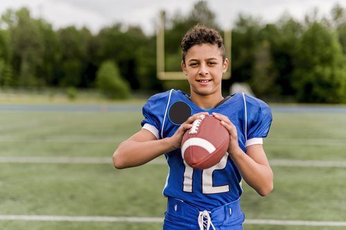 Boy in blue football uniform holding a football on a green field.