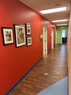 Red hallway with framed photos on the left, wood-look floor, and doors. Green exit sign at the end.
