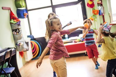 Children dancing and playing with musical instruments in a colorful classroom.