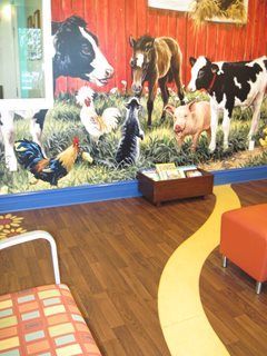 Barnyard mural with farm animals; reading area with yellow path on wood floor, orange ottoman, and colorful chair.