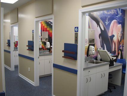 Hallway with dental exam rooms. Rooms have countertops, sinks, and whimsical murals.