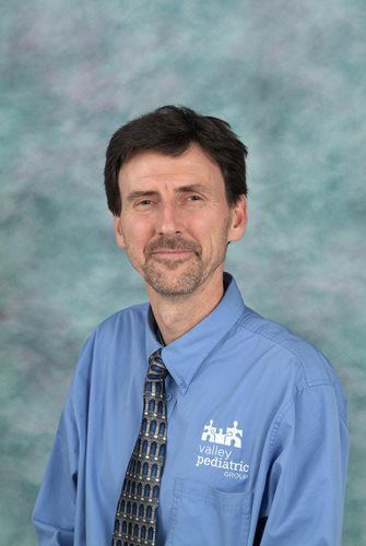 Man in blue shirt and tie, smiling. The shirt has