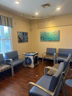 Waiting room with blue chairs, artwork on walls, and a decorative table.