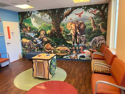 Children's waiting room with a jungle mural. Orange chairs, wooden toy, and blue walls.