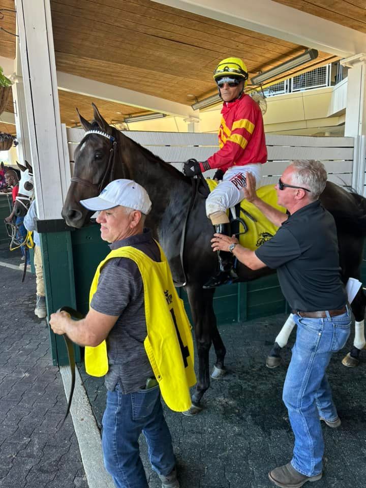 A jockey is riding a horse with two men standing next to it.