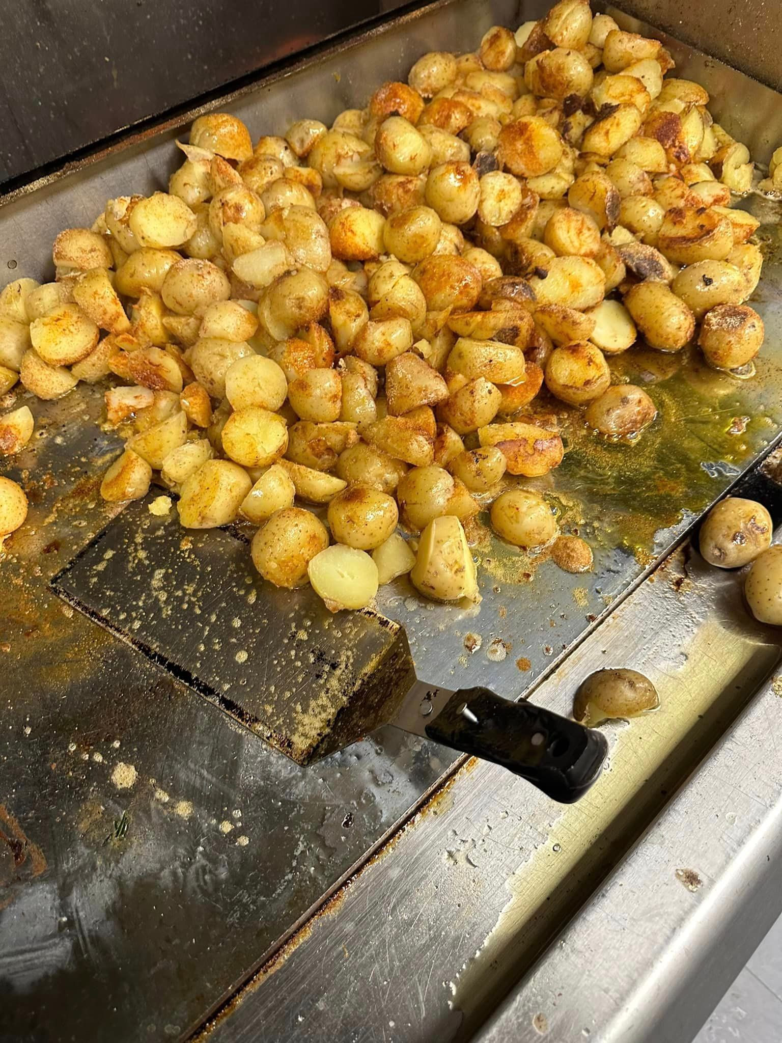 Potatoes are being cooked on a grill with a spatula.