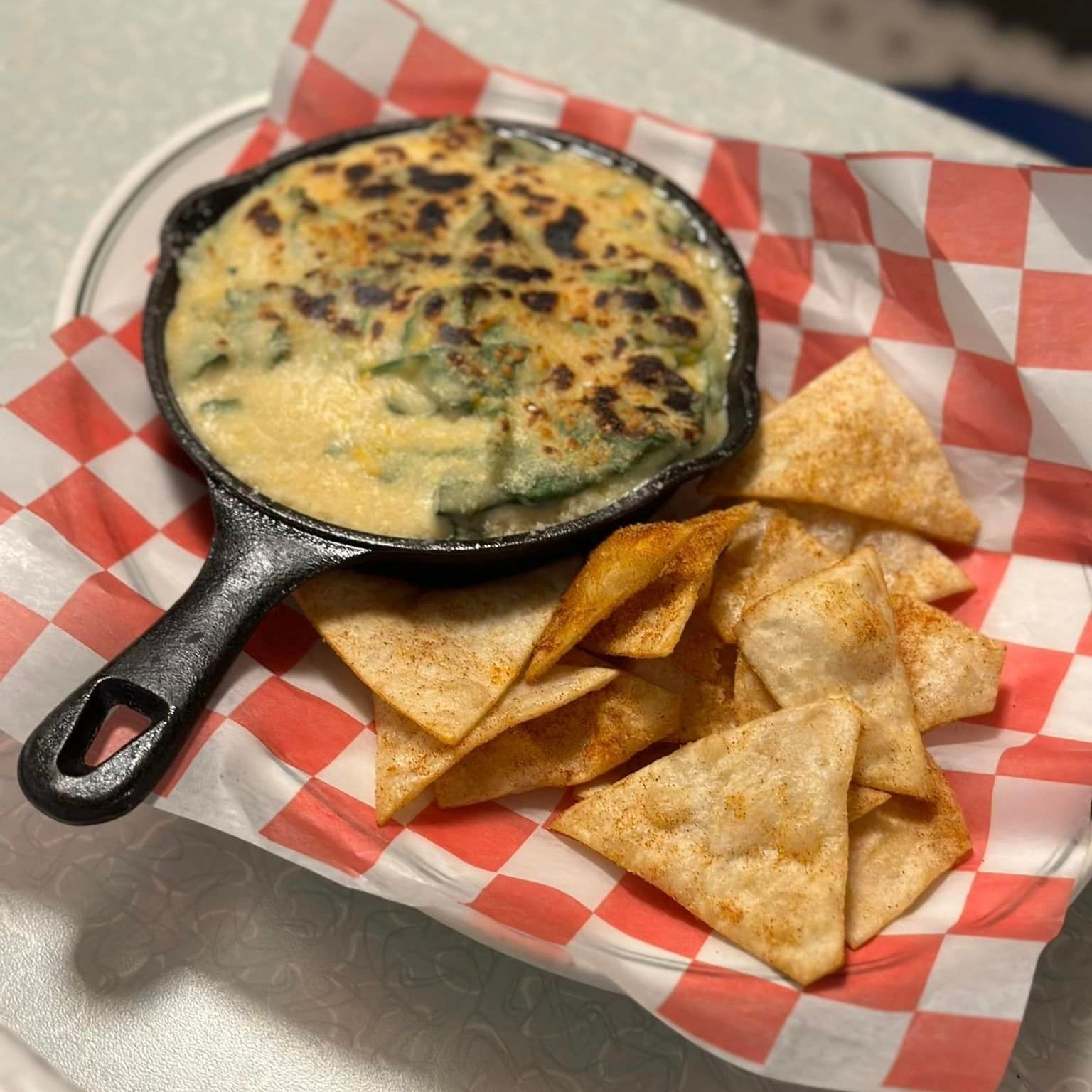 A skillet of dip and tortilla chips on a checkered paper