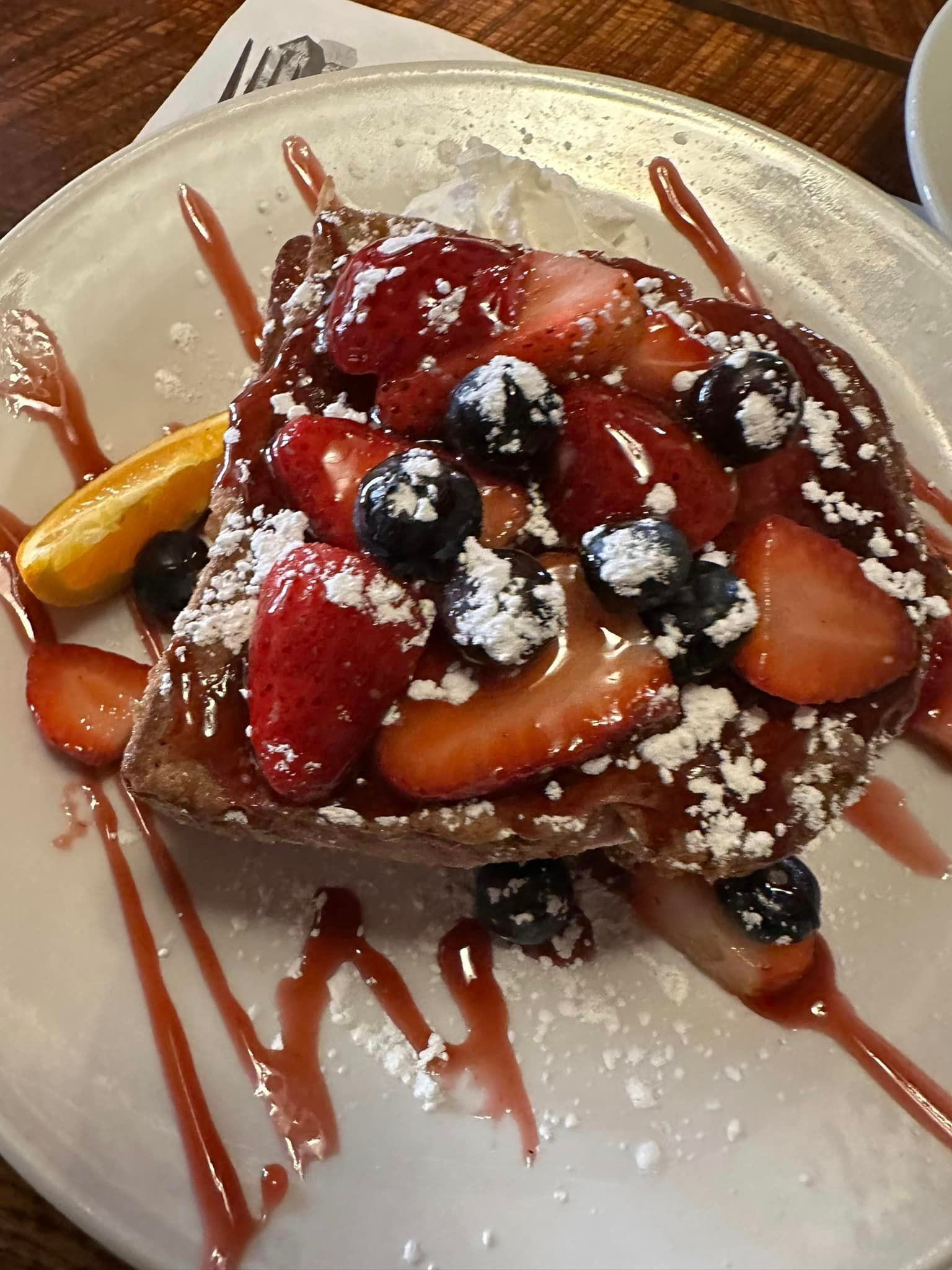 A slice of french toast with strawberries and blueberries on a white plate.