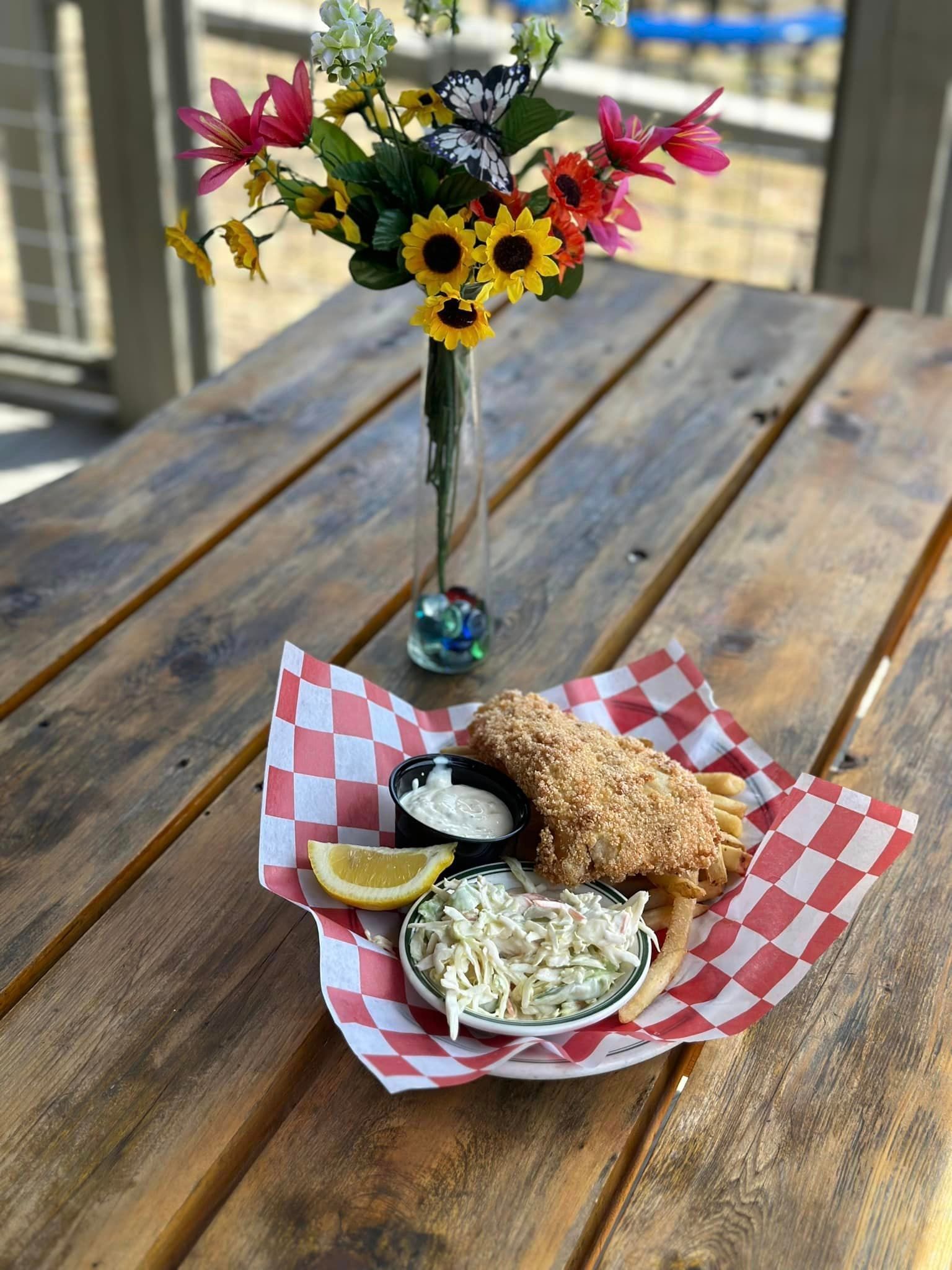 A wooden table topped with a basket of food and a vase of flowers.
