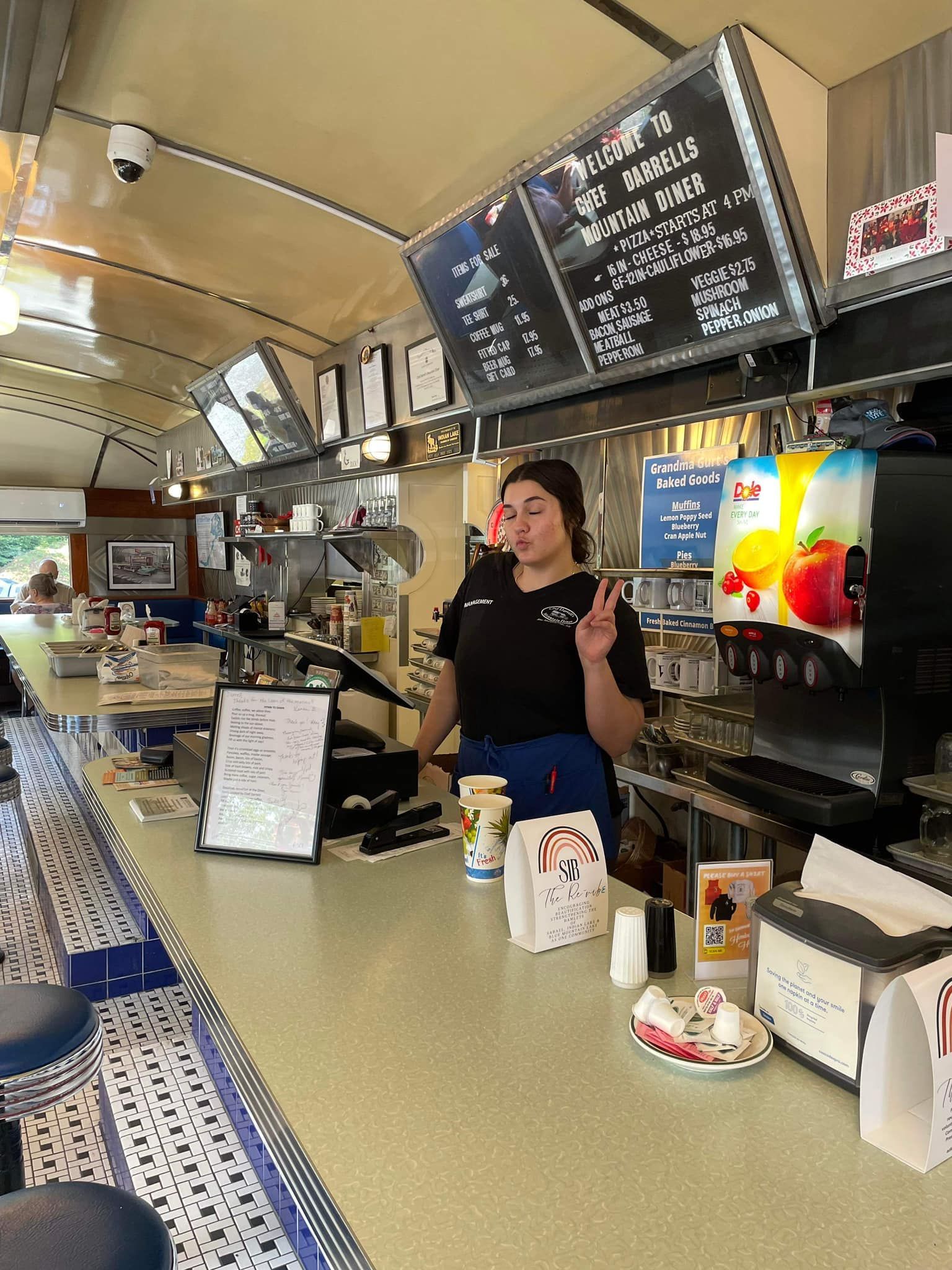A woman is standing behind a counter in a diner giving a peace sign.
