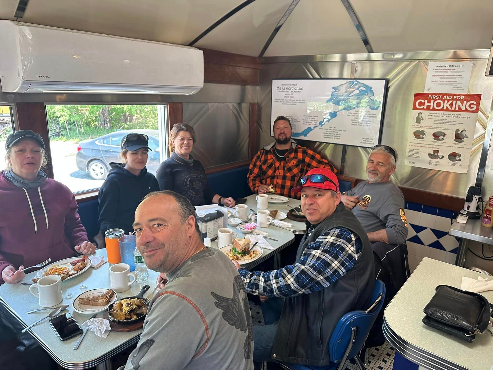 A group of people are sitting at a table in a diner eating food.