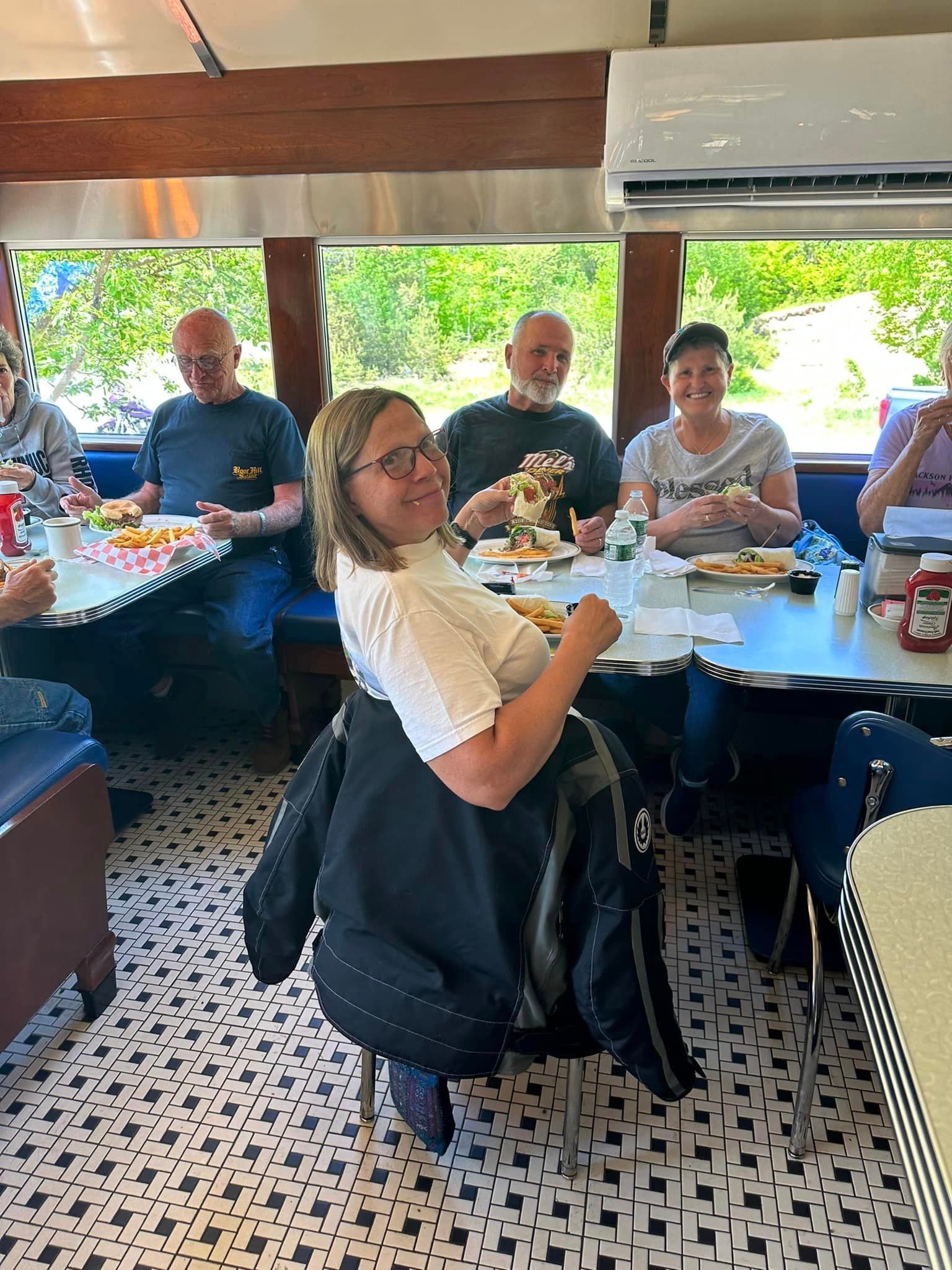 A group of people are sitting at tables in a diner eating food.