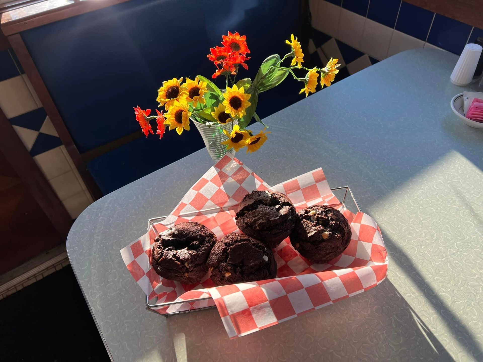 A basket of chocolate donuts sits on a table next to a vase of flowers