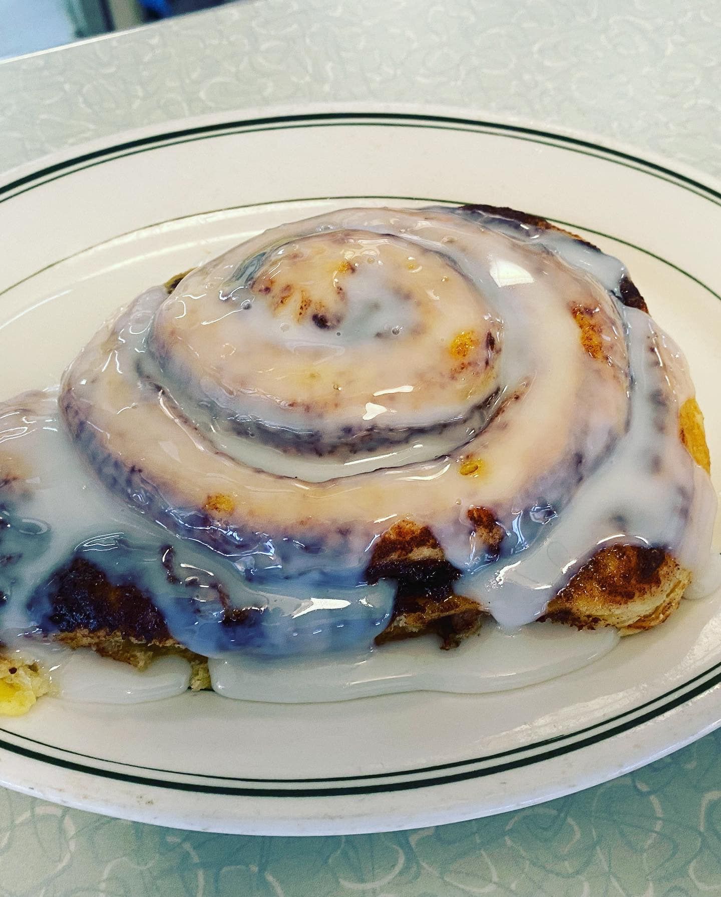 A cinnamon roll with icing on a white plate