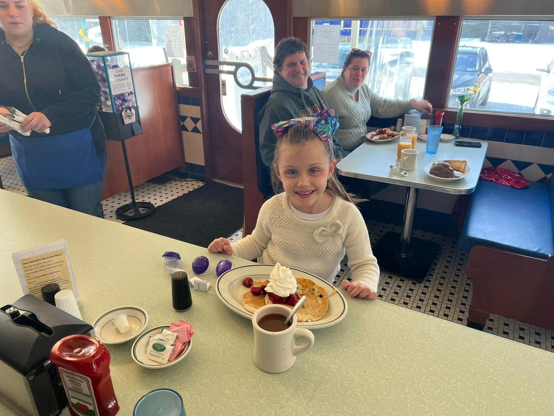 A little girl is sitting at a table with a plate of pancakes and a cup of coffee.