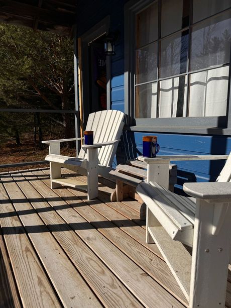 Two white chairs are sitting on a wooden porch in front of a blue house.