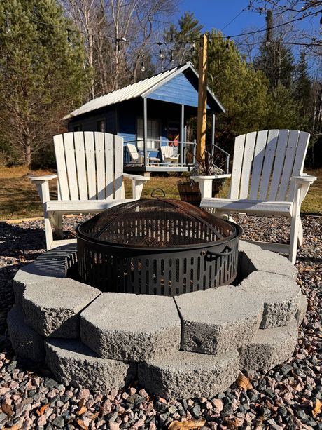 Two chairs are sitting around a fire pit in front of a small house.