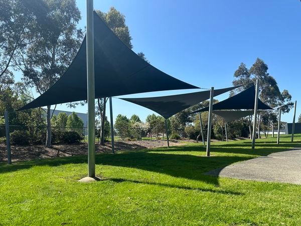 Shade sail installation at Casey RACE Swimming Pool Centre, 65 Berwick-Cranbourne Rd, Cranbourne East VIC 3977—featuring vibrant blue and white linked rectangular hyperbolic canopies stretched over an outdoor pool area, supported by powder-coated steel posts, with sun loungers and landscaping visible beneath a clear sky