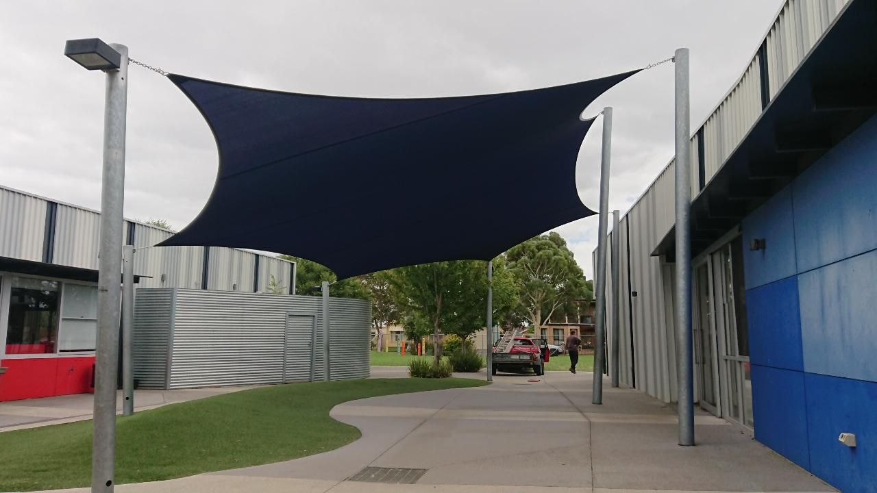 Shade sail installation at St Francis de Sales Primary School, 122 Paterson Dr, Lynbrook VIC 3975—featuring a durable dark blue canopy supported by steel posts, providing sun protection for students in the vibrant schoolyard surrounded by modern architecture and lush greenery