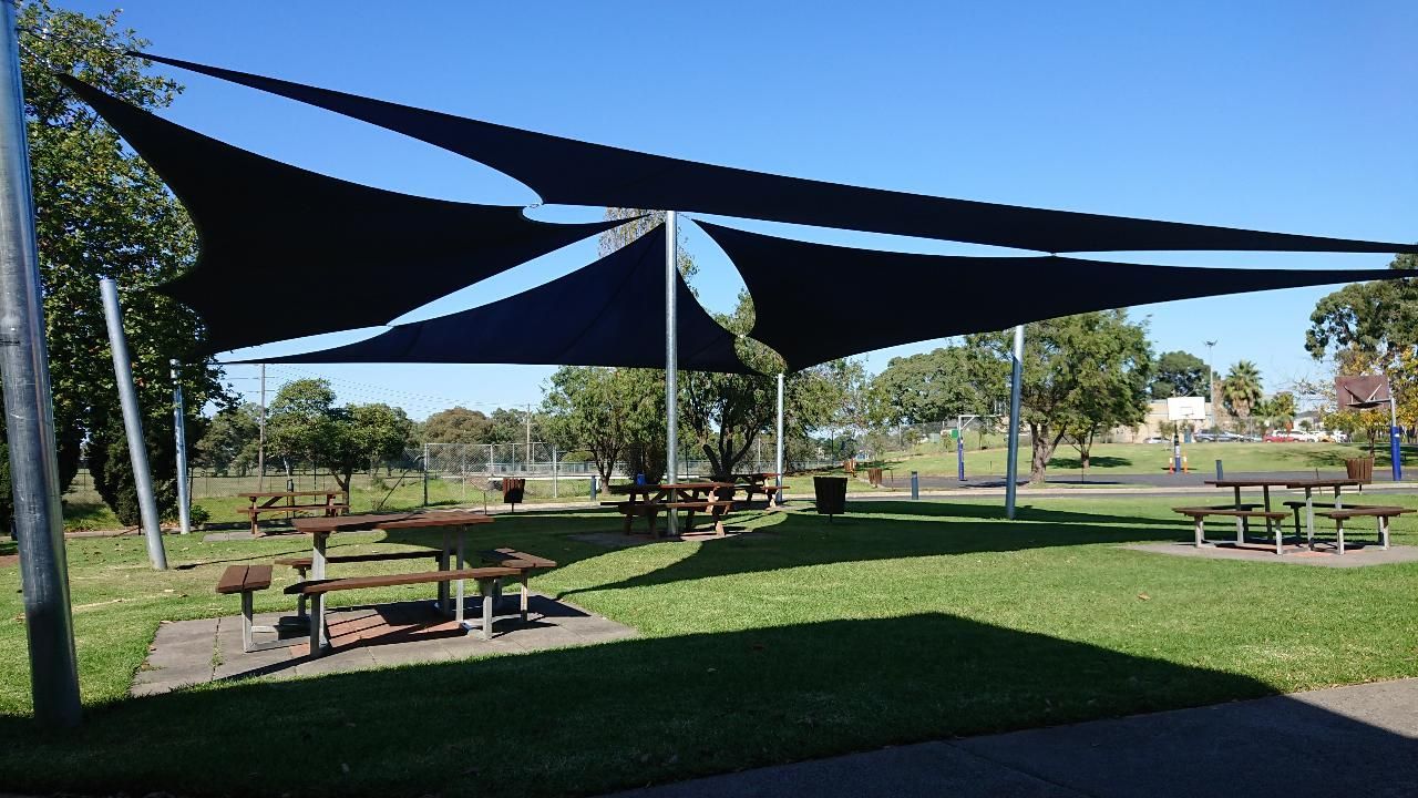 Shade sail installation at Lynbrook Primary School, 37 Paterson Dr, Lynbrook VIC 3975—featuring a blue and white canopy supported by metal posts, providing sun protection over outdoor picnic tables near a brick school building in a grassy courtyard