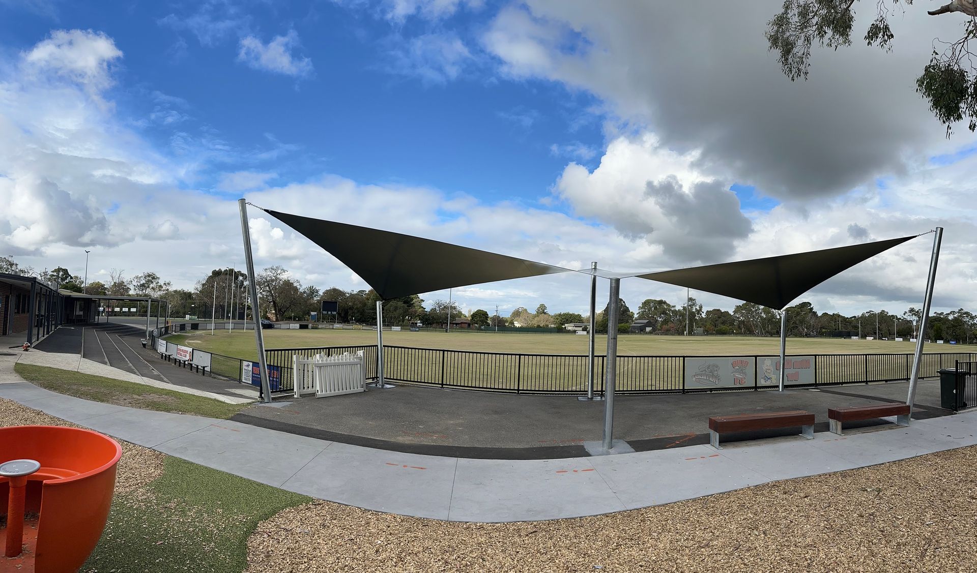 Spectator shade sail installation at Devon Meadows Football and Netball Club—featuring a modern canopy supported by sturdy steel posts, covering bench seating bar area along the field with a clear view of the playing area for the community 