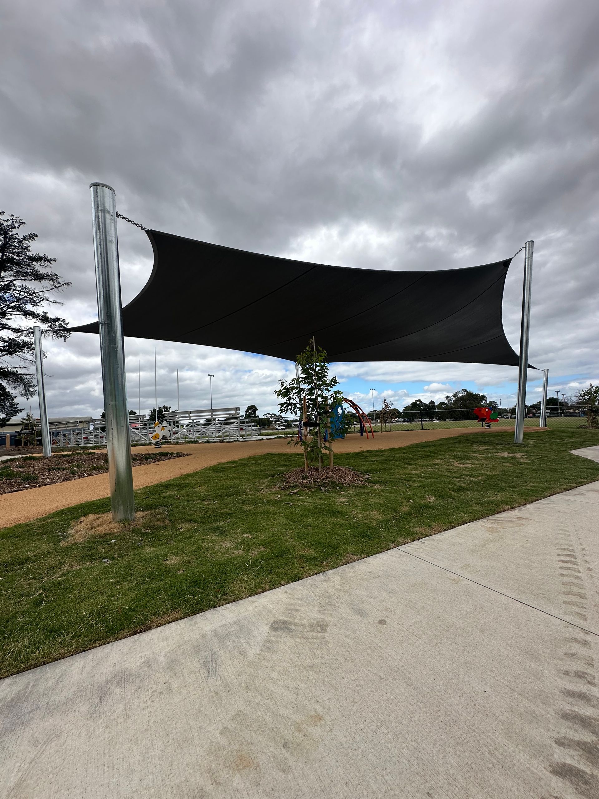 UV-protective shade sail structure over public play area at Pearcedale Recreation Reserve, featuring landscaped borders and playground equipment for early childhood use