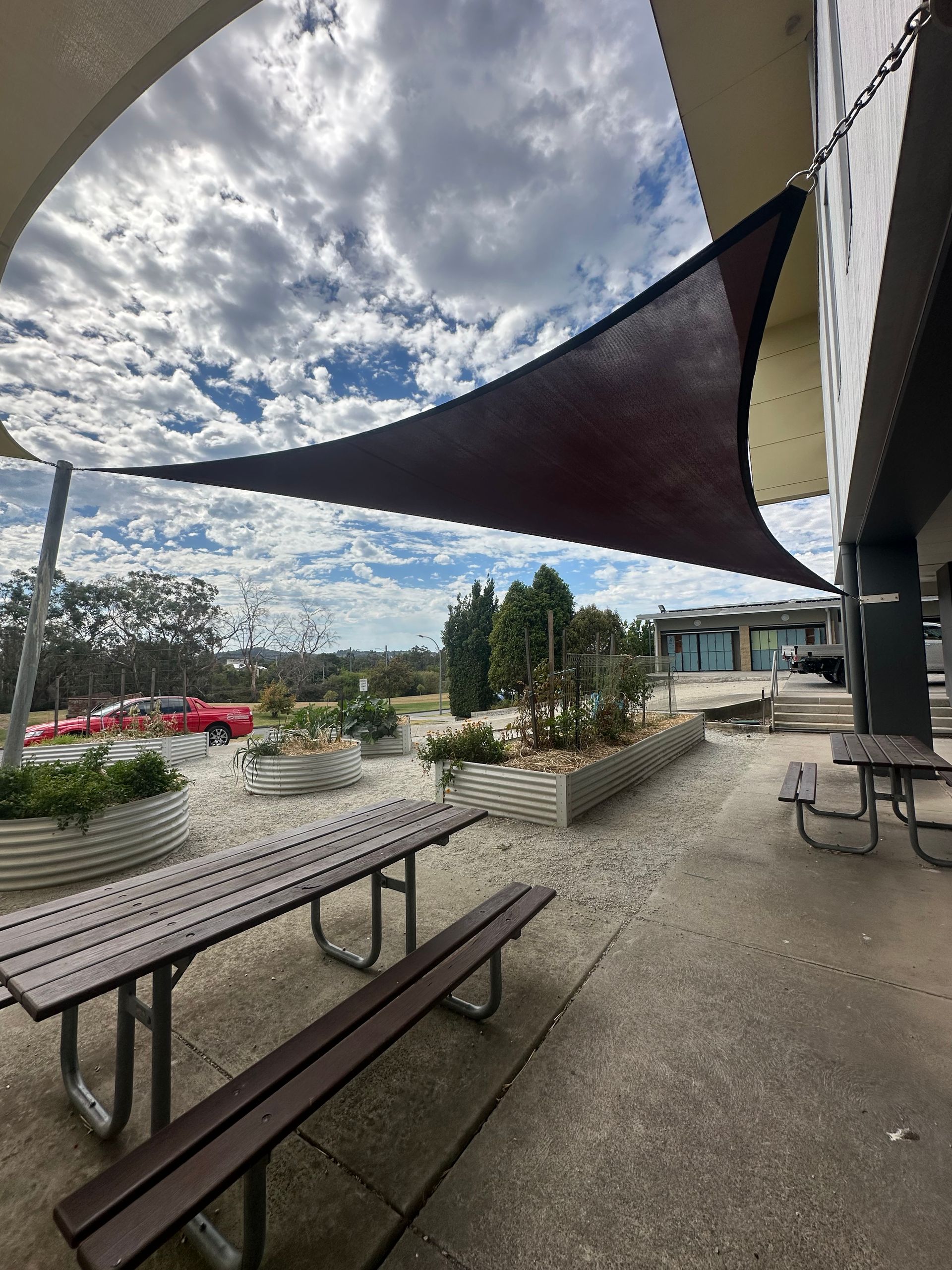 Custom shade sail canopy system covering outdoor amphitheatre at Beaconhills College in Berwick, featuring tensioned fabric in blue and beige tones over landscaped green play space with surrounding educational facilities.