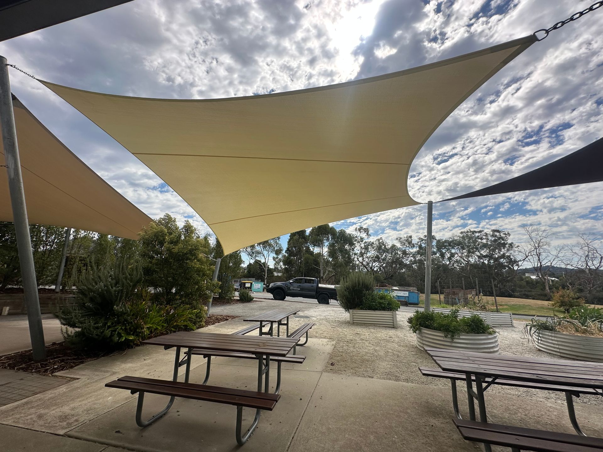 Custom shade sail canopy system covering outdoor amphitheatre at Beaconhills College in Berwick, featuring tensioned fabric in blue and beige tones over landscaped green play space with surrounding educational facilities.