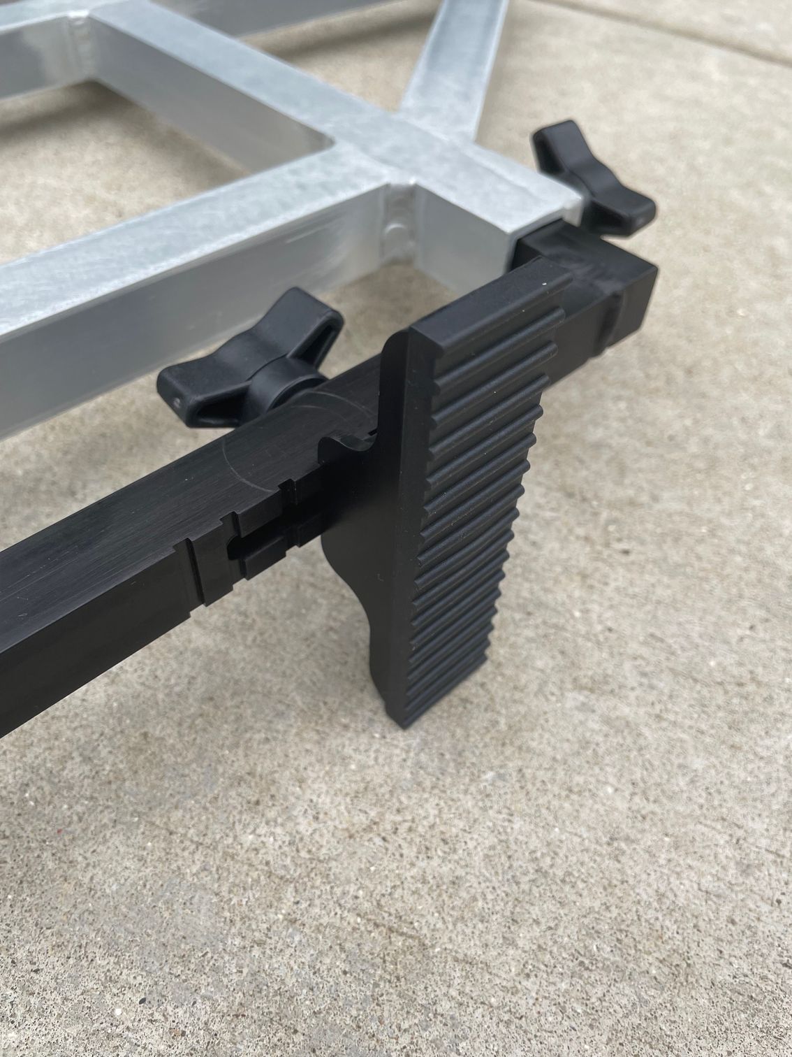 Black adjustable leg on a silver aluminum structure, resting on concrete.