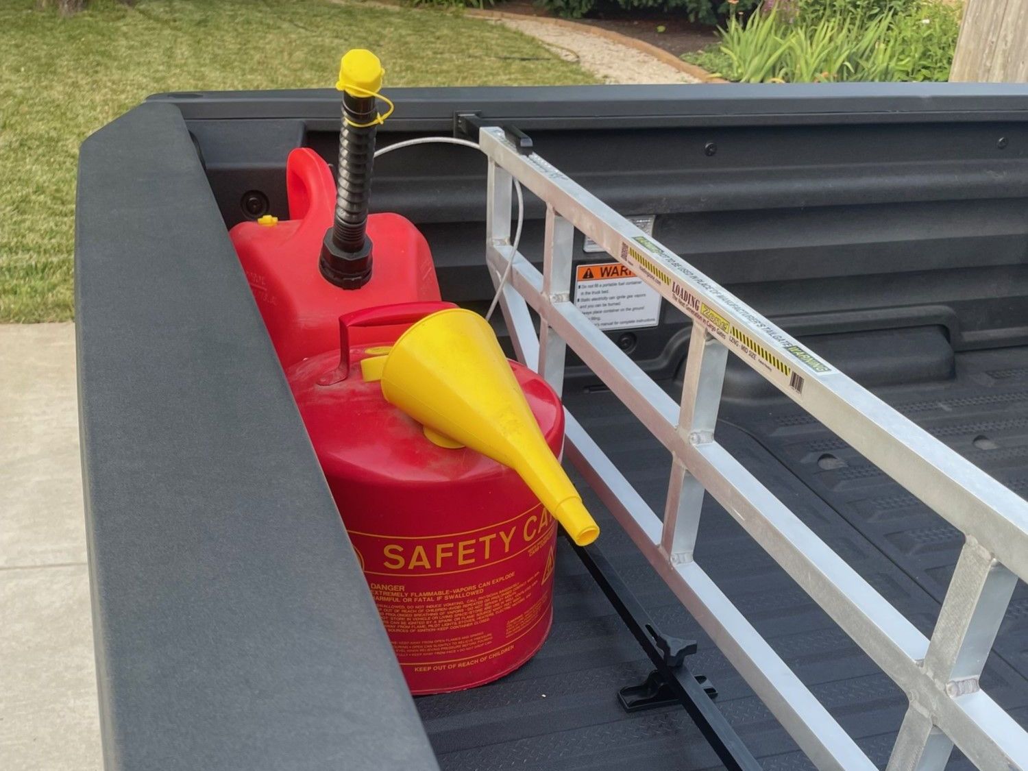 Red gas can with funnel in truck bed, near a ladder-like divider. Yellow cap on gas can.