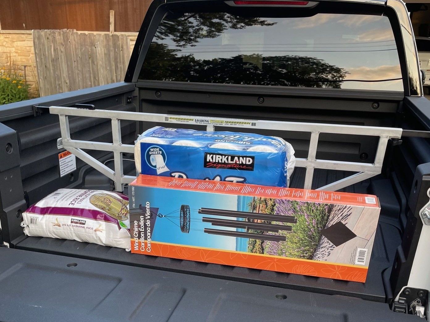Truck bed with a cargo divider holding groceries, including toilet paper and a tripod box.