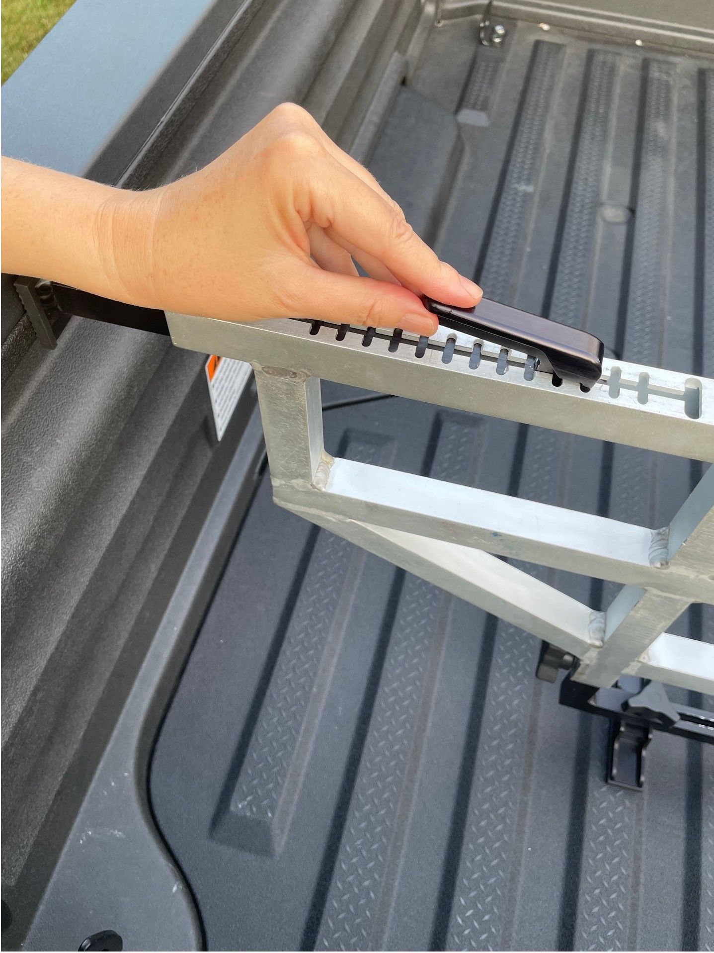 Hand placing a black object on a silver metal rack inside a truck bed.