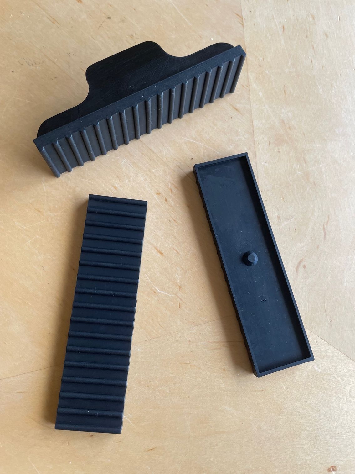 Three black rubber parts with ribbed surfaces on a wooden surface.