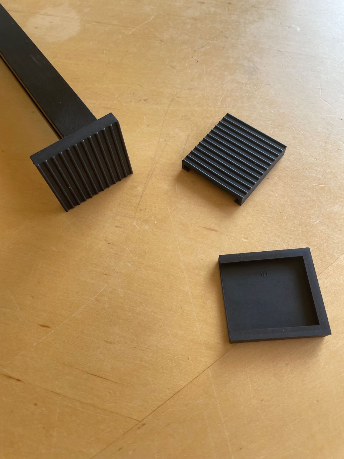 Black rubber furniture feet on a wooden surface, with a flat piece in the background.
