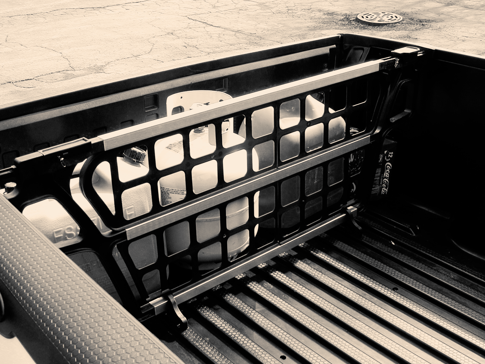 Black truck bed cargo divider holding a propane tank and gas cans.