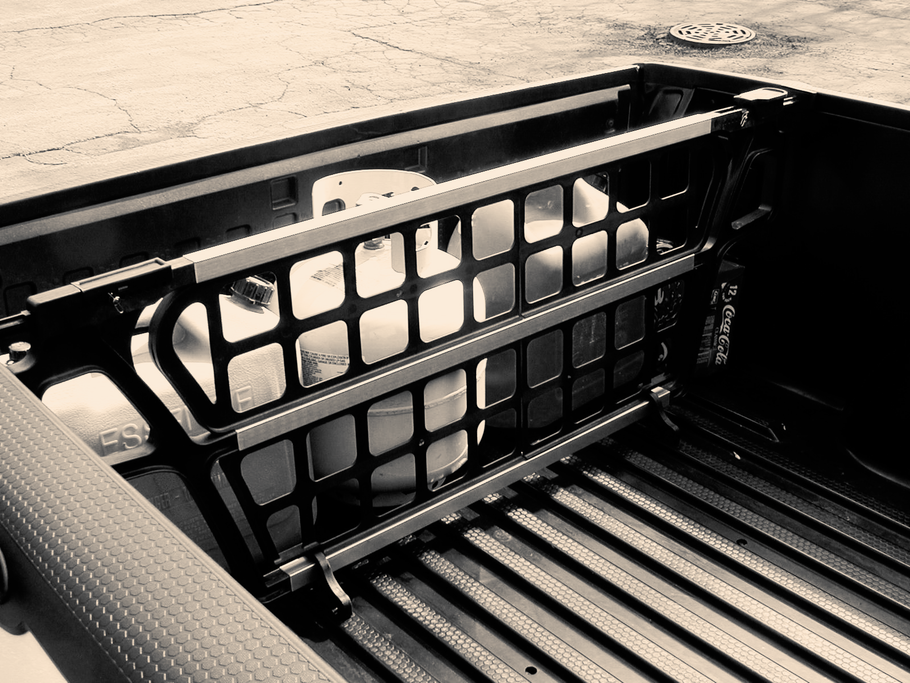 Black truck bed cargo divider holding a propane tank and gas cans.