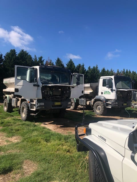 Two Dump Trucks Are Parked Next To Each Other In A Grassy Field — B & W Commercials In Wauchope, NSW