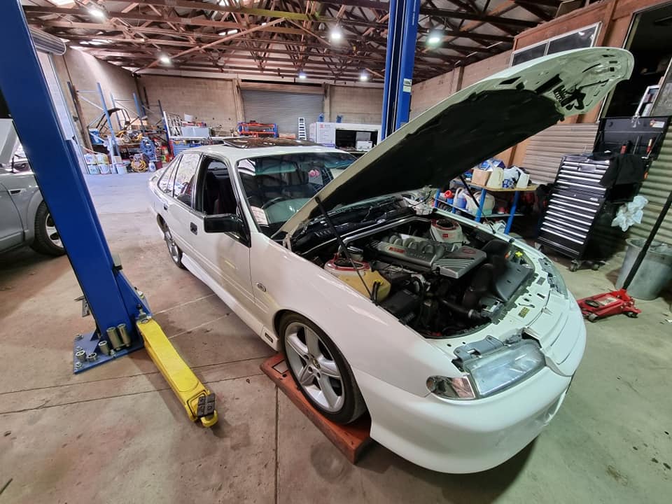 A White Car With The Hood Open Is On A Lift In A Garage — B & W Commercials In Wauchope, NSW