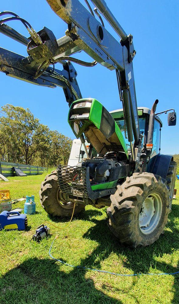 A Green And Black Tractor With Its Hood Open Is Parked In A Grassy Field — B & W Commercials In Wauchope, NSW