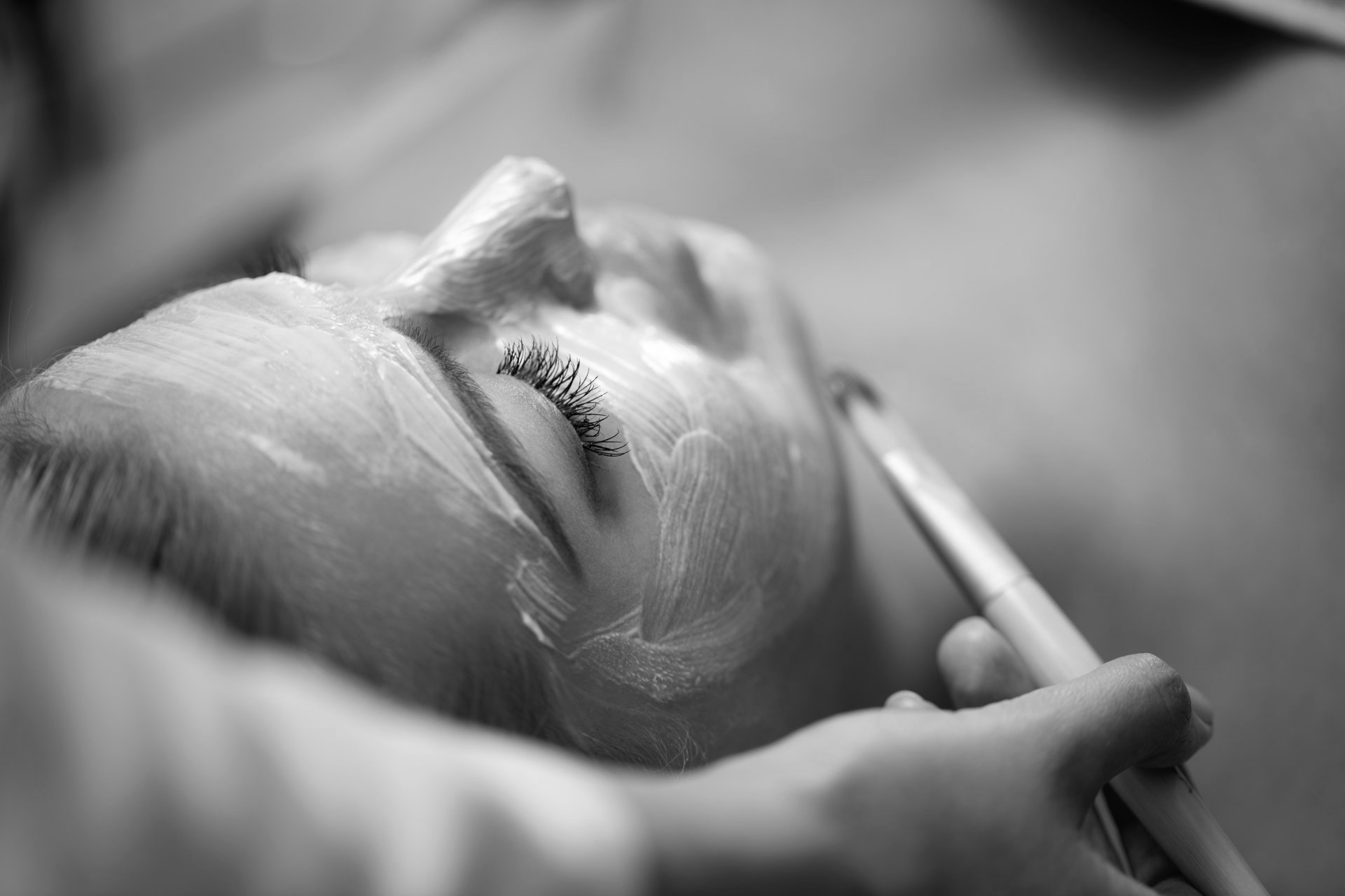 A woman is getting a facial treatment in a black and white photo.