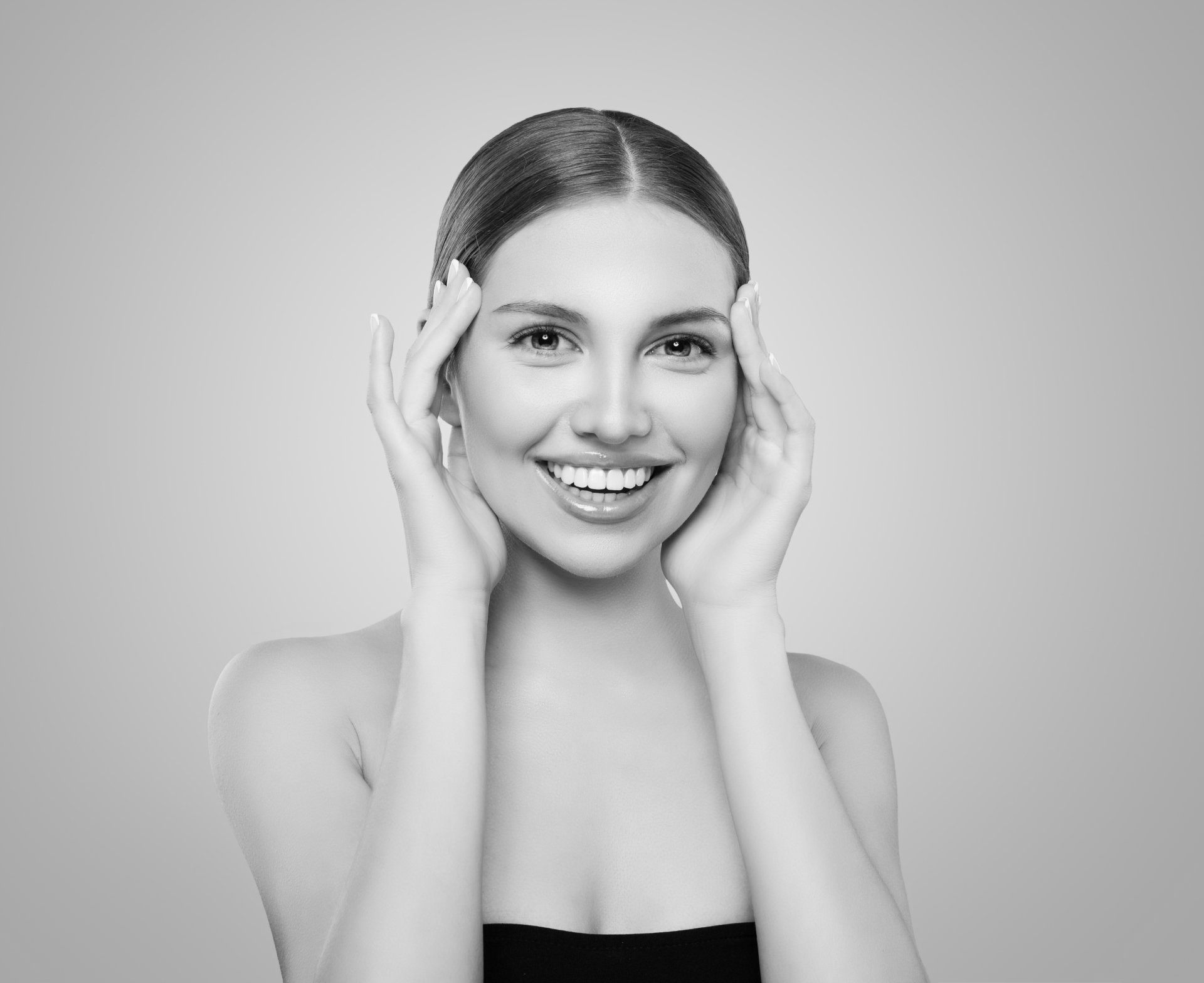A black and white photo of a smiling woman touching her face.