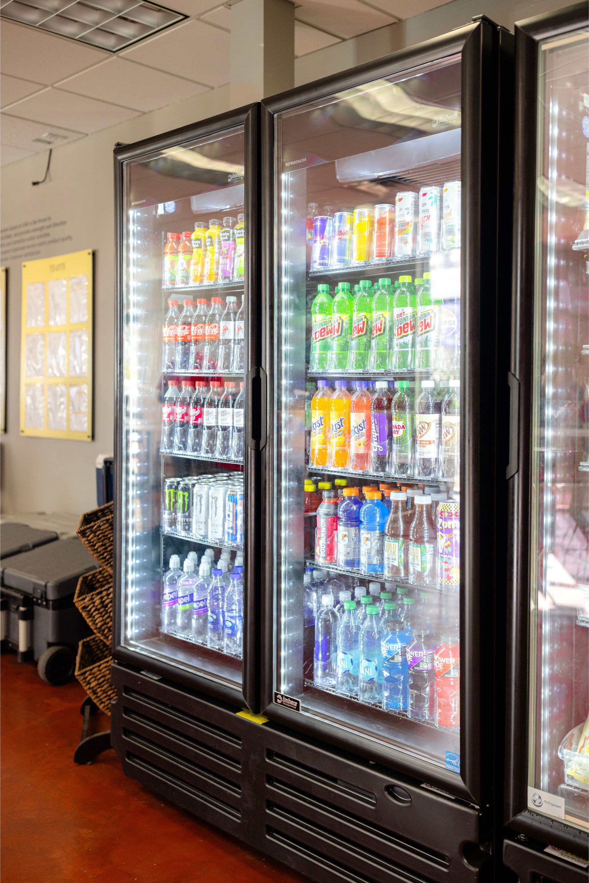 Two glass-front refrigerators stocked with various colorful bottled beverages in a brightly lit, commercial setting.