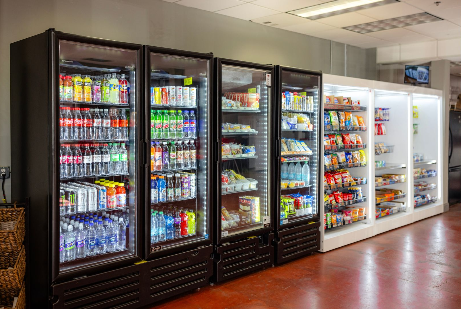 A row of glass-front commercial refrigerators filled with various beverages and packaged snacks in a well-lit store.