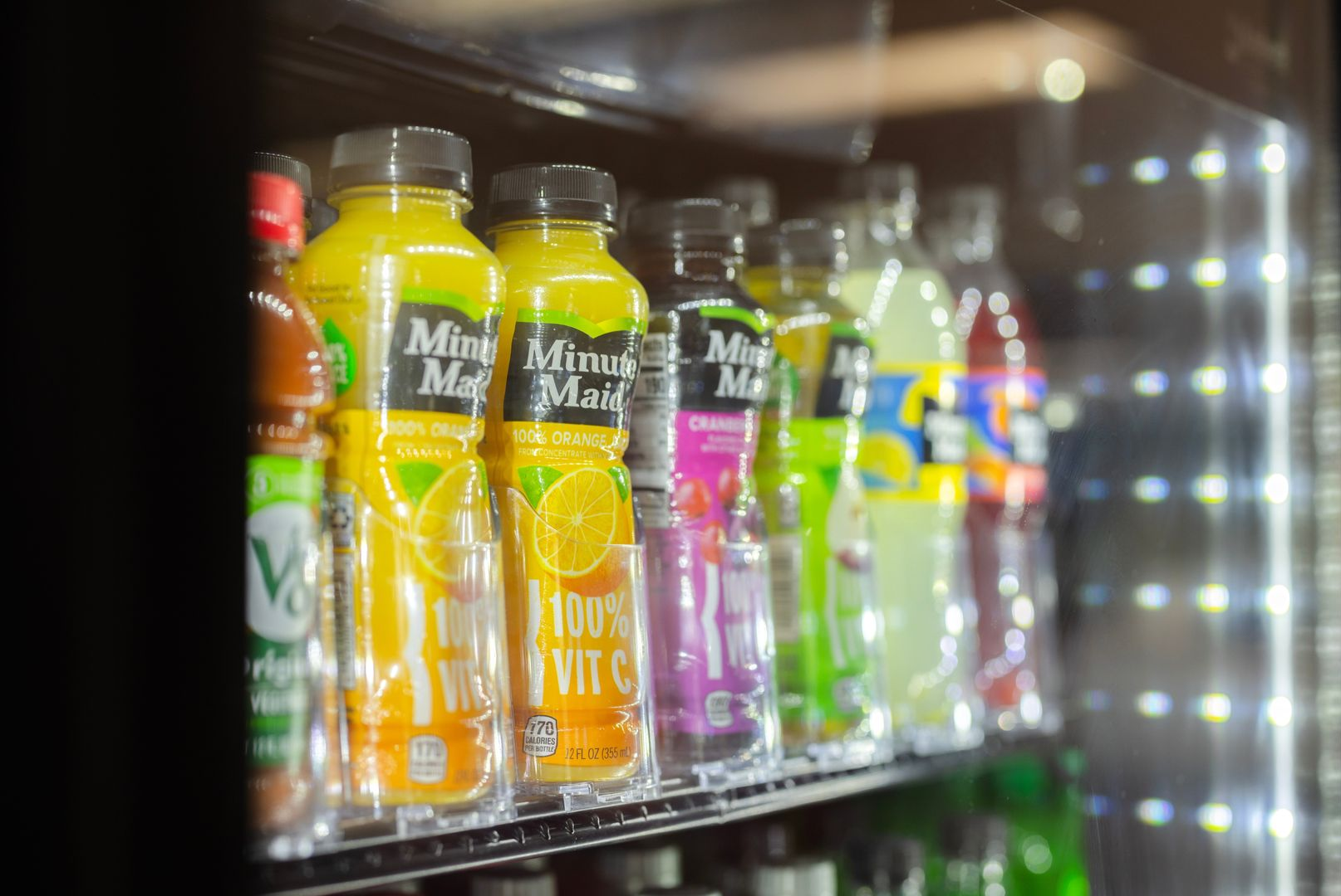 A refrigerated display case shelf stocked with various bottles of Minute Maid juice and other assorted drinks.