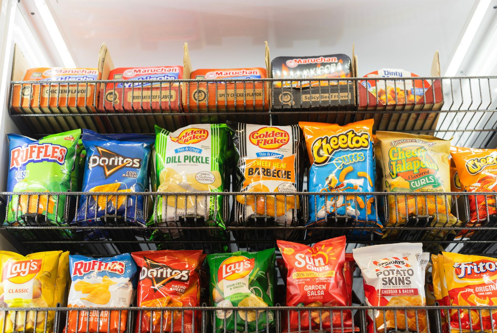 A retail display shelf filled with rows of various bagged snacks, including Doritos, Cheetos, and Lay's.