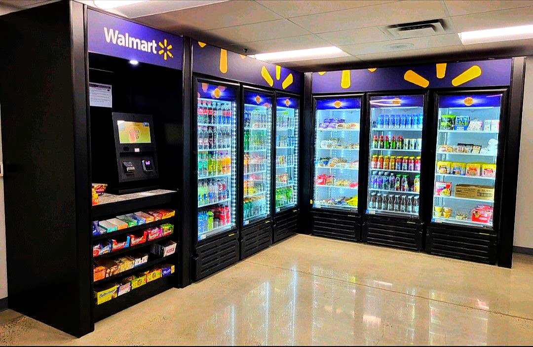 A Walmart-branded vending machine station featuring a touch screen kiosk and multiple glass-door snack and drink coolers.