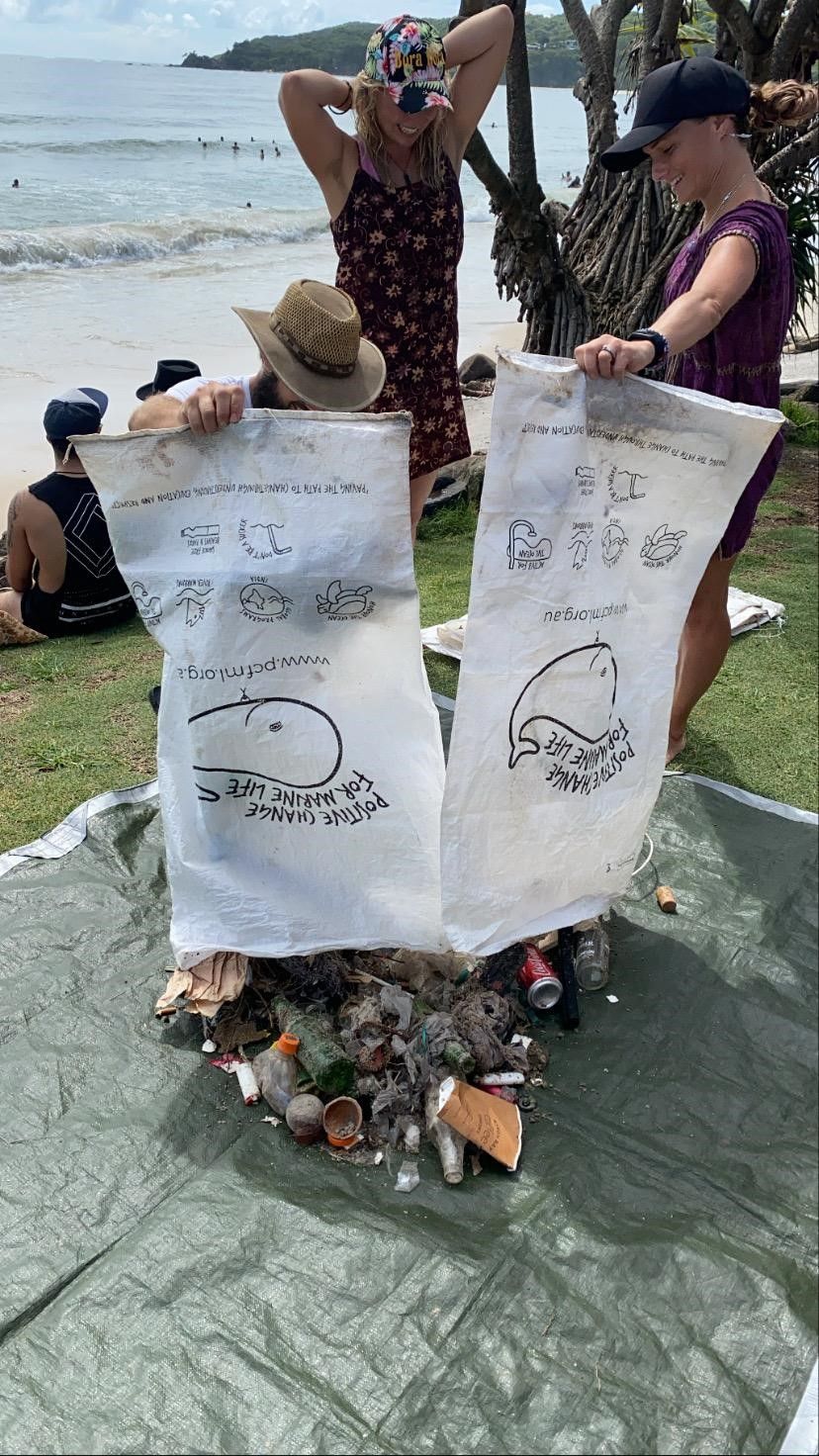 A group of people are standing around a pile of trash on a beach.