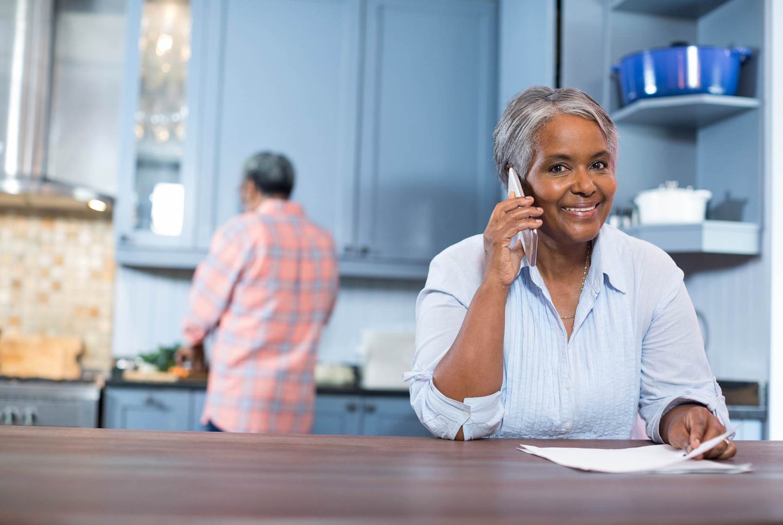 A woman is sitting at a kitchen counter talking on a cell phone.