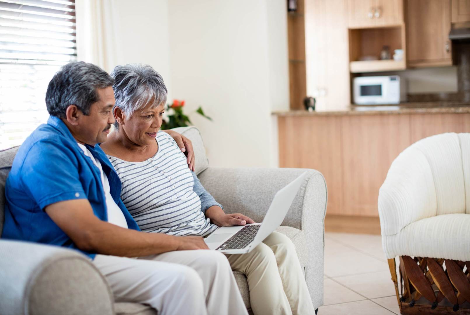 An elderly couple is sitting on a couch looking at a laptop.